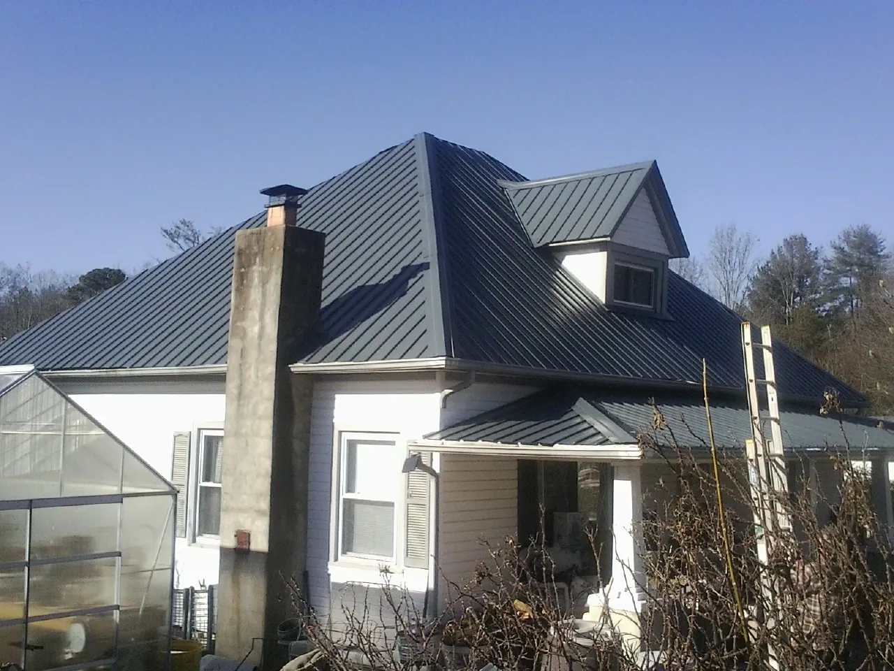 Dark blue standing seam metal roof on a white farmhouse with dormer — Slate & Tile Roof Repair by Roofing Brothers in Oglesby