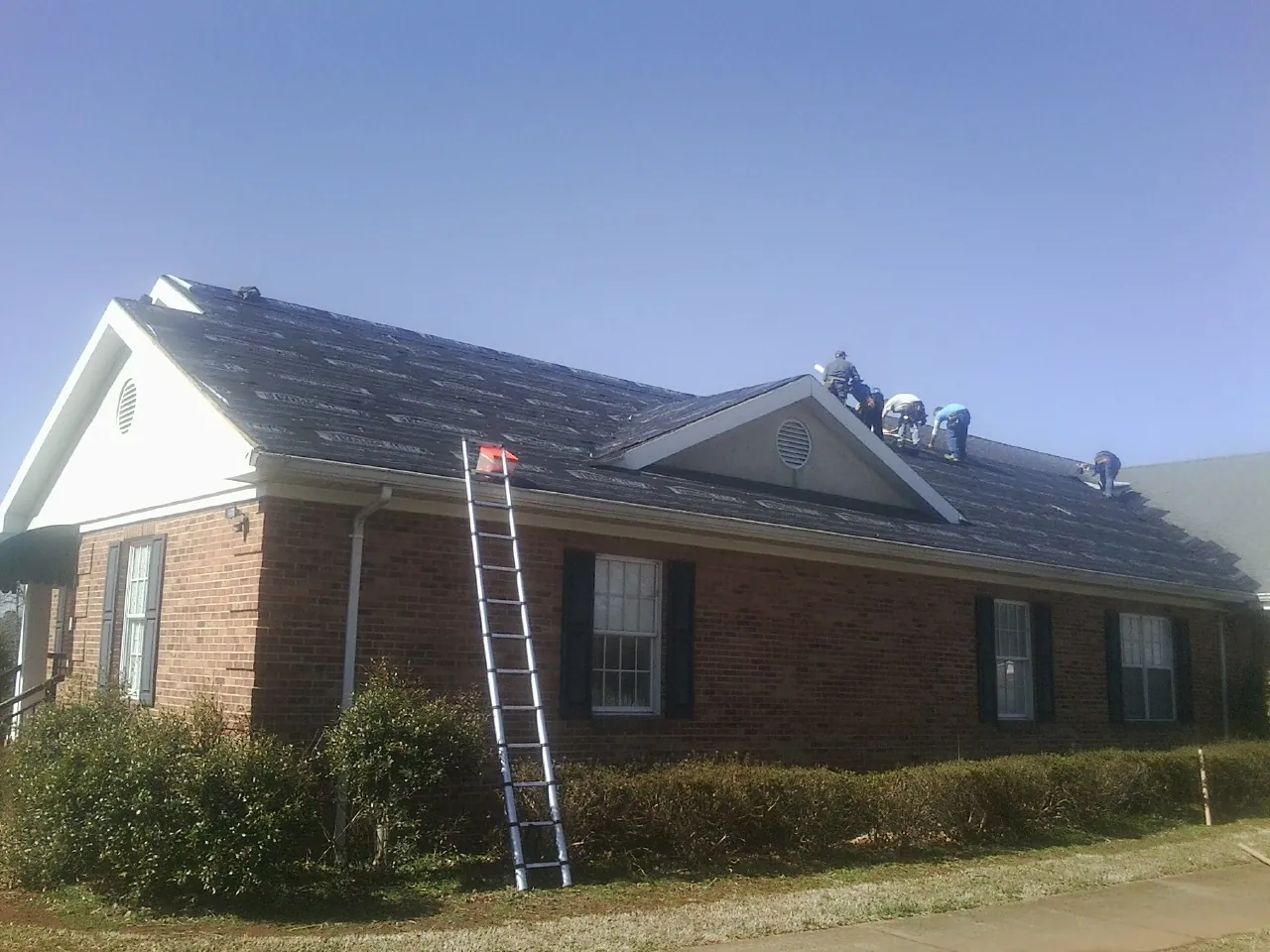 Crew tearing shingles off a brick ranch roof with a ladder set — Emergency Roof Repair work by our crew in Oglesby