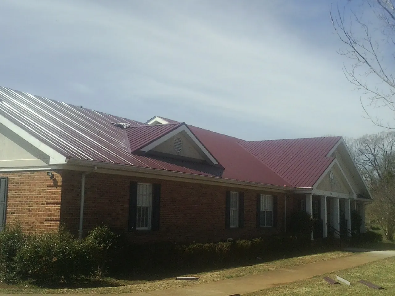 Red metal roof with gabled entries on a long brick building, from a Hail Damage Roof Repair job in Oglesby