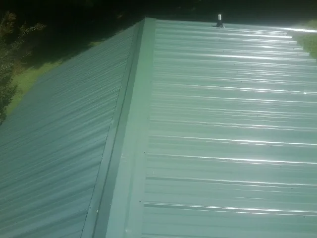 New green metal panels meeting at the ridge of a roof — Flat Roof Repair work by our crew in Oglesby
