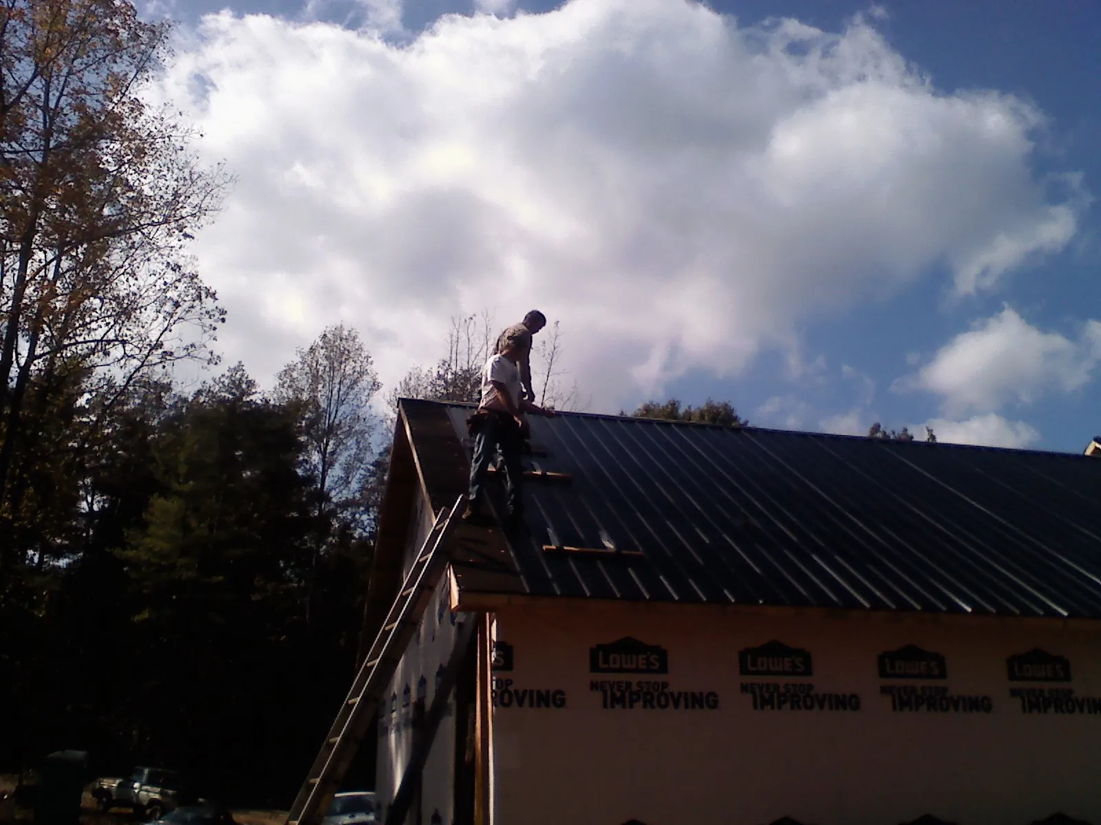Roofer fastening dark metal panels high against a cloudy sky, from a Roof Inspection job in Oglesby