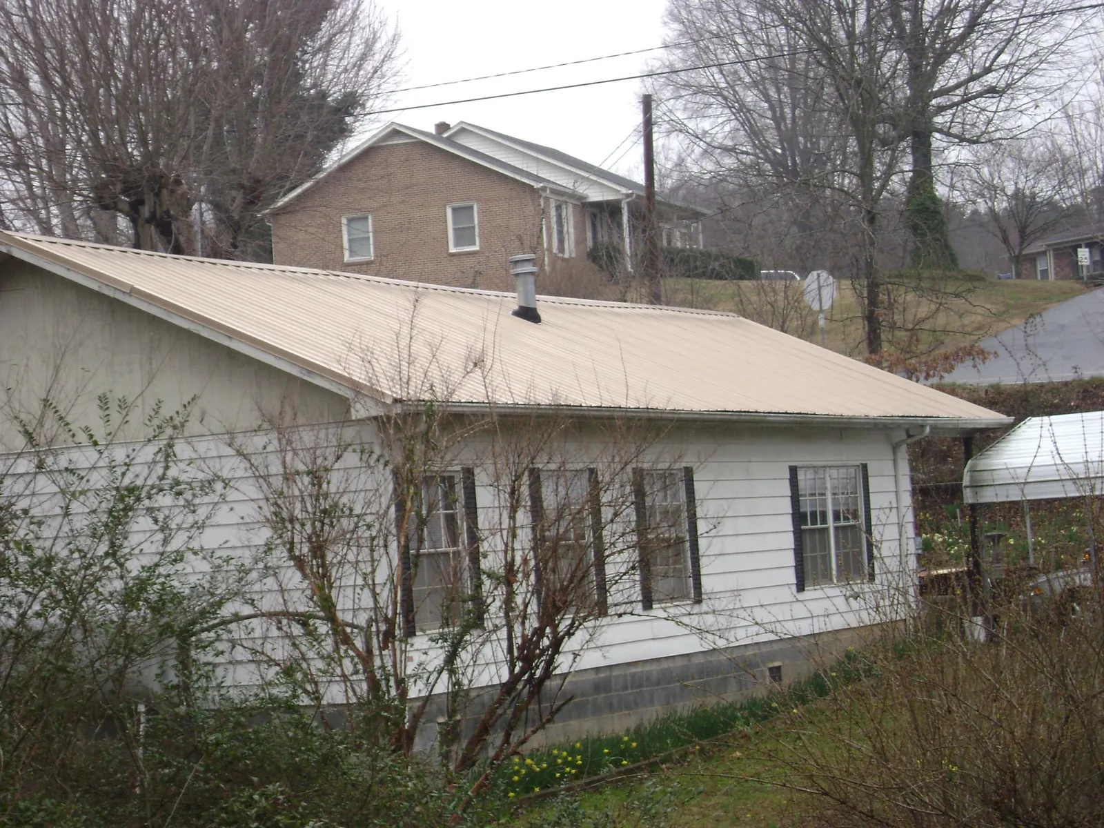 Tan metal roof on a white sided house set into a hillside — Commercial Roofing by Roofing Brothers in Oglesby