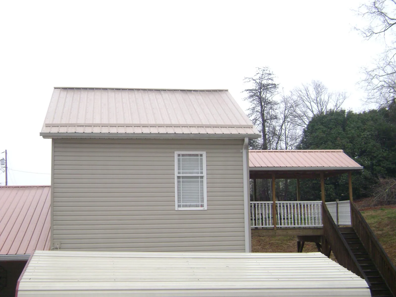 Tan metal roofs on a two story addition and attached porch, from a Roof Replacement job in Oglesby